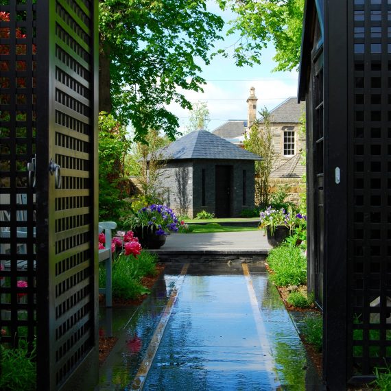 View through side garden to stone and slate garden building, designed by Carolyn Grohmann